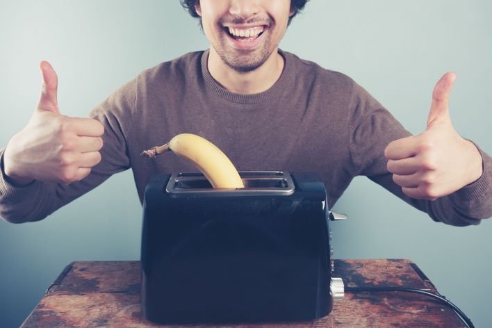 A young man is toasting a banana and giving thumbs up